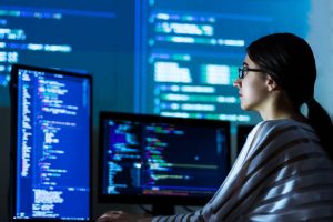 Software developer writing code in front of multiple monitors