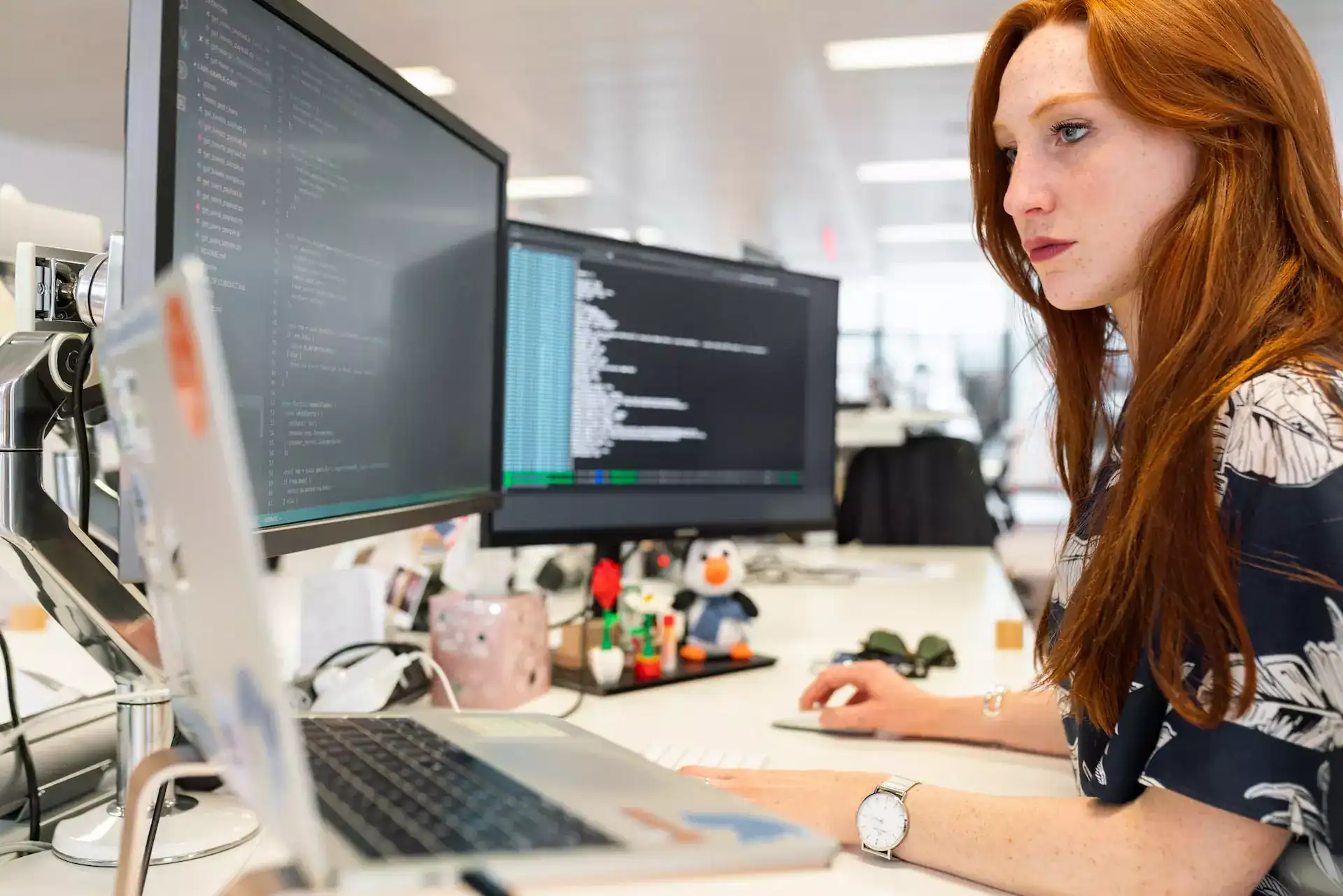 A Developer sitting at a desk in front of laptop and monitor screens and coding