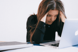 Person holding their head while looking stressed at a laptop on a desk.